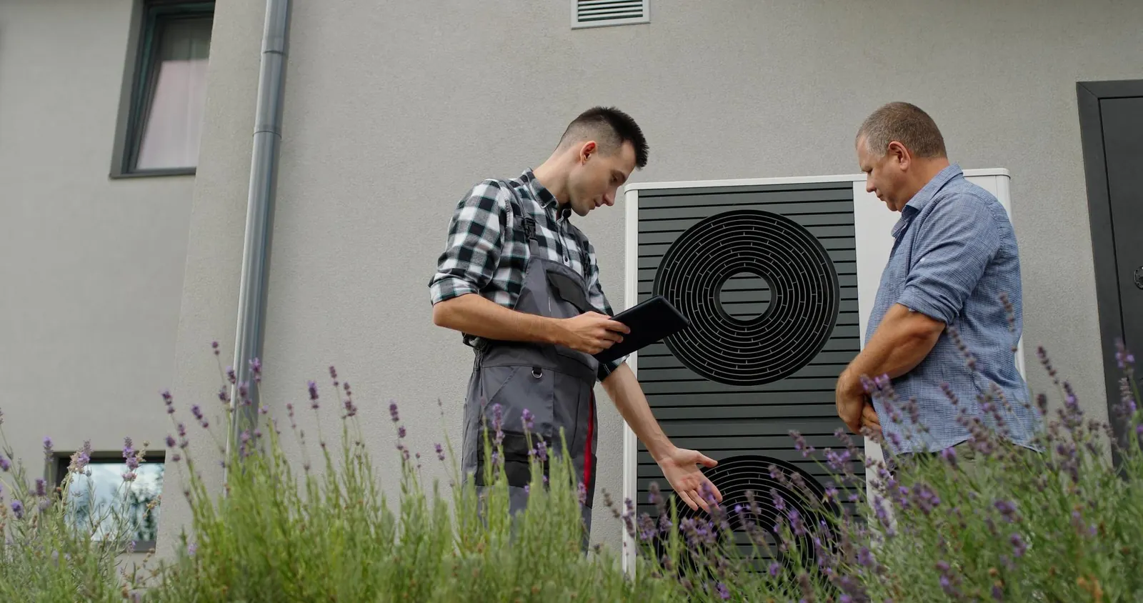 Technicien conseillant un propriétaire sur une pompe à chaleur avec tablette